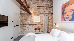 A bedroom with a brick wall, a bed, a chair, a radiator, and a painting. -  5star central zone1 -2 bed 2 bath Slps 6 superWifi  (London)