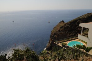 A cliffside property with a swimming pool, overlooking a coastal ocean with sailboats. - Villa Belo Horizonte (Caniço)
