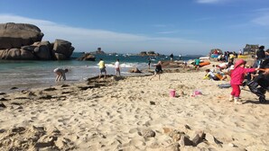 Ein Sandstrand mit großen Felsen und Menschen, die unterschiedliche Aktivitäten ausüben.