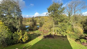 Ein grasbewachsener Bereich mit einem Kiesweg, der zu einem Teich führt, umgeben von Bäumen und einem Steinzaun.