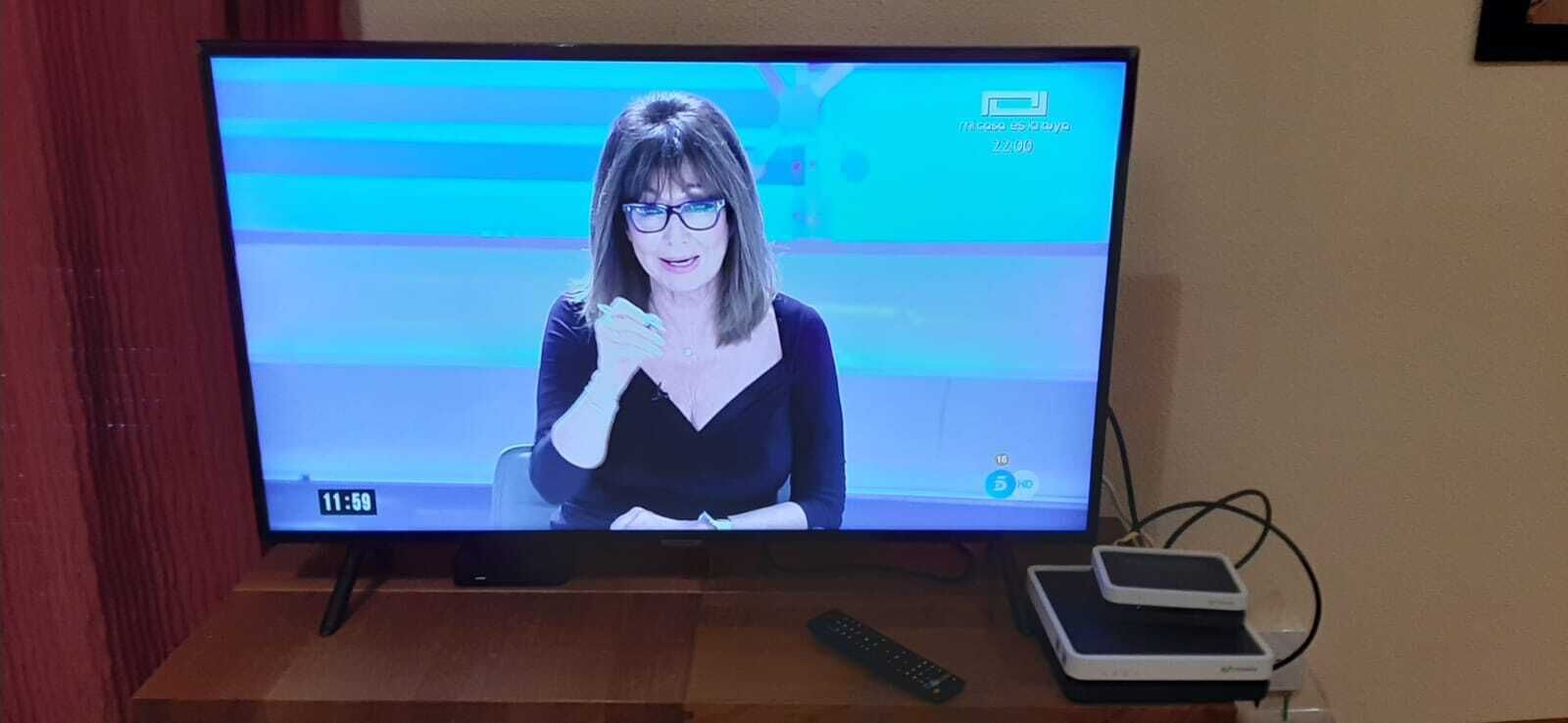 A television displaying a news anchor, a remote control, and a streaming device on a stand.