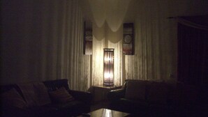 A dimly lit room with a large window covered by sheer curtains, a standing lamp, and two sofas. - Beautiful villa with heated pool, large patio area and barbecue (Fuerteventura)