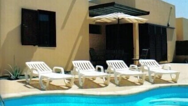 A poolside area with white lounge chairs and a canopy umbrella. - Beautiful villa with heated pool, large patio area and barbecue (Fuerteventura)