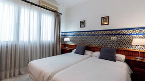Ett hotellrum med en stor säng, två sängbord, ett litet bord, en väggmonterad luftkonditioneringsanläggning och ett väggkakel med ett mönster bakom sängen.