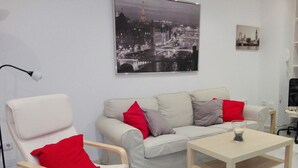 Een woonkamer met een witte bank, rode en grijze kussens, een houten salontafel en een zwarte vloerlamp.