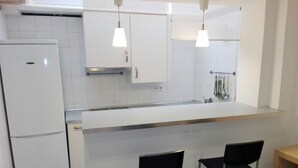 Een keuken met witte kastjes, een witte koelkast, twee zwarte barkrukken en hanglampen.