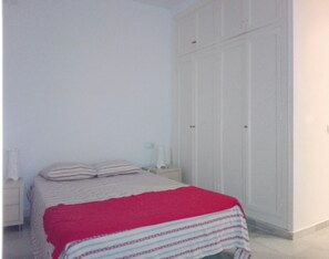 Een slaapkamer met een bed, nachtkastje, kast en een rode deken.