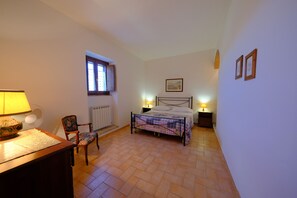 A bedroom with a bed, a chair, a desk, a window, and two wall-mounted picture frames.