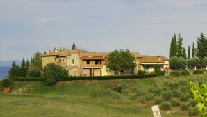 Uma casa grande, de vários andares, com telhado de telhas, rodeada por vegetação e árvores.