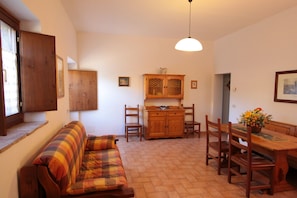 Een gezellige woonkamer met een bank, een houten eettafel, stoelen en een kast.
