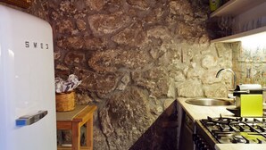 Una cocina con pared de piedra, refrigerador blanco, pileta y cocina a gas.