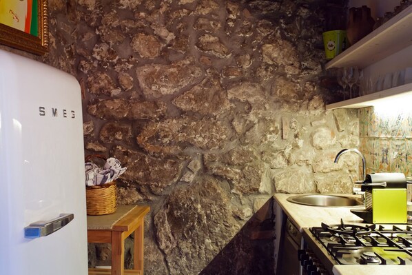 Una cucina con parete in pietra, frigorifero bianco, lavello e piano cottura a gas.