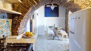 Una cocina con un arco de piedra que da a un comedor. Hay una estufa, un plato con limones y una mesa lista para comer.
