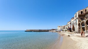 Una playa costera con aguas cristalinas, un muelle de piedra y edificios tradicionales a lo largo de la orilla.