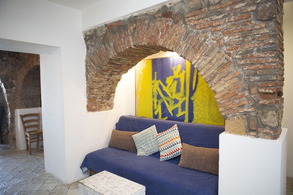 A room with a brick archway, a blue sofa with patterned cushions, and a yellow abstract painting on the wall.