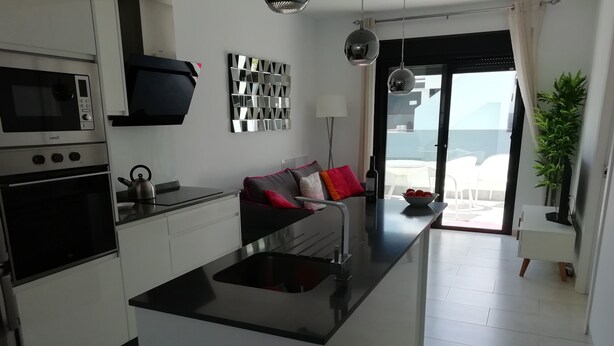 Una cocina moderna con una isla central, horno empotrado, microondas y un comedor con sofá y mesa.