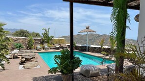 Zona de piscina con sillones de descanso, una pérgola y vistas a las montañas.