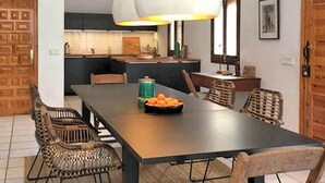 Un comedor con una mesa larga, sillas de mimbre y un cuenco de fruta.