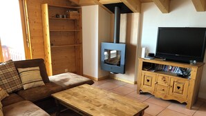 A cozy living room with a wooden sofa, a coffee table, a TV stand with a flat-screen TV, and a wood-burning stove.