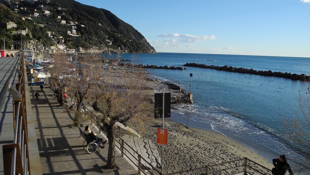 Une promenade en bord de mer avec un sentier pavé, une plage et une digue rocheuse.