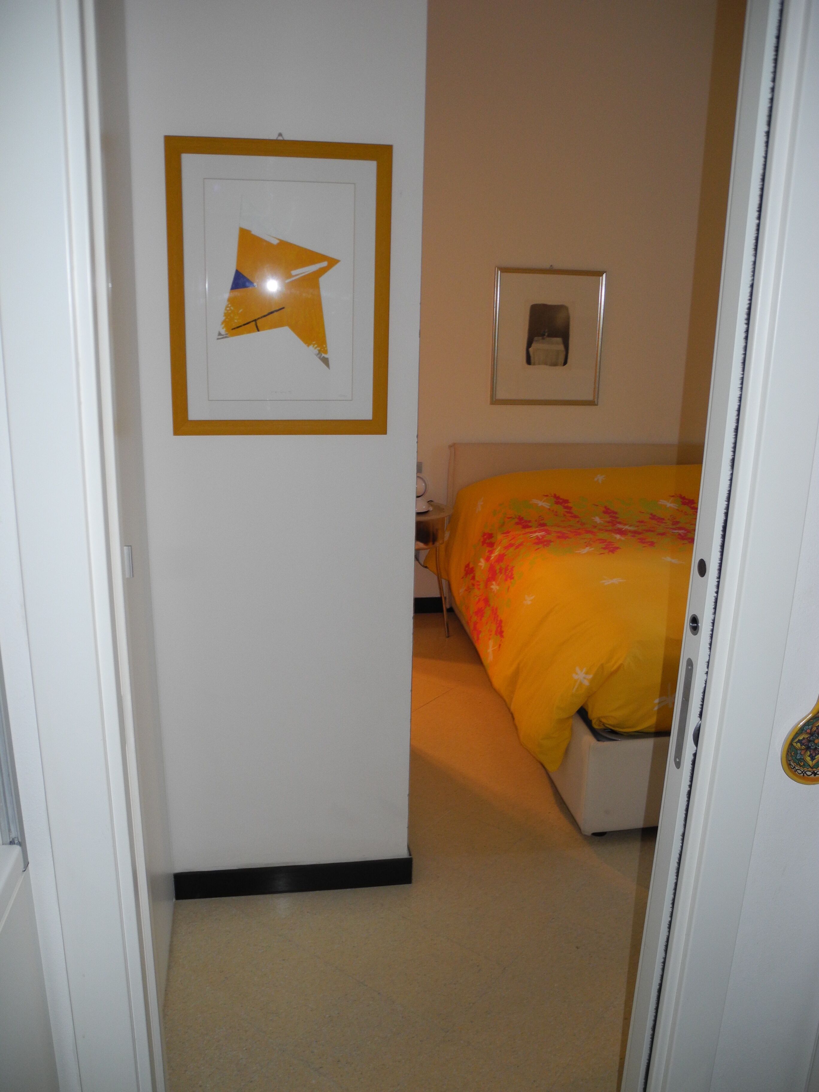 Un dormitorio con cama, un cuadro enmarcado en la pared y una puerta que da a otra habitación.