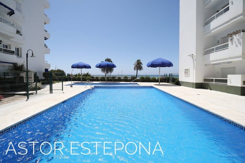Ein Swimmingpool mit blauem Wasser, umgeben von weißen Gebäuden und blauen Sonnenschirmen.