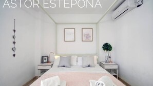 A hotel room with a bed, two bedside tables, a wall-mounted air conditioner, and a framed picture on the wall. - Astor Estepona: Lux 2BD Frontline Marina, Pool, WiFi, Sea views, Private parking (Estepona)