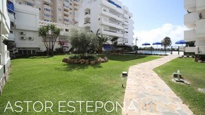 A courtyard with a stone pathway, a small garden area, and a pool in the background. - Astor Estepona: Lux 2BD Frontline Marina, Pool, WiFi, Sea views, Private parking (Estepona)