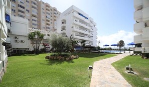 Un patio con un camino de piedra, un pequeño jardín y una piscina al fondo.