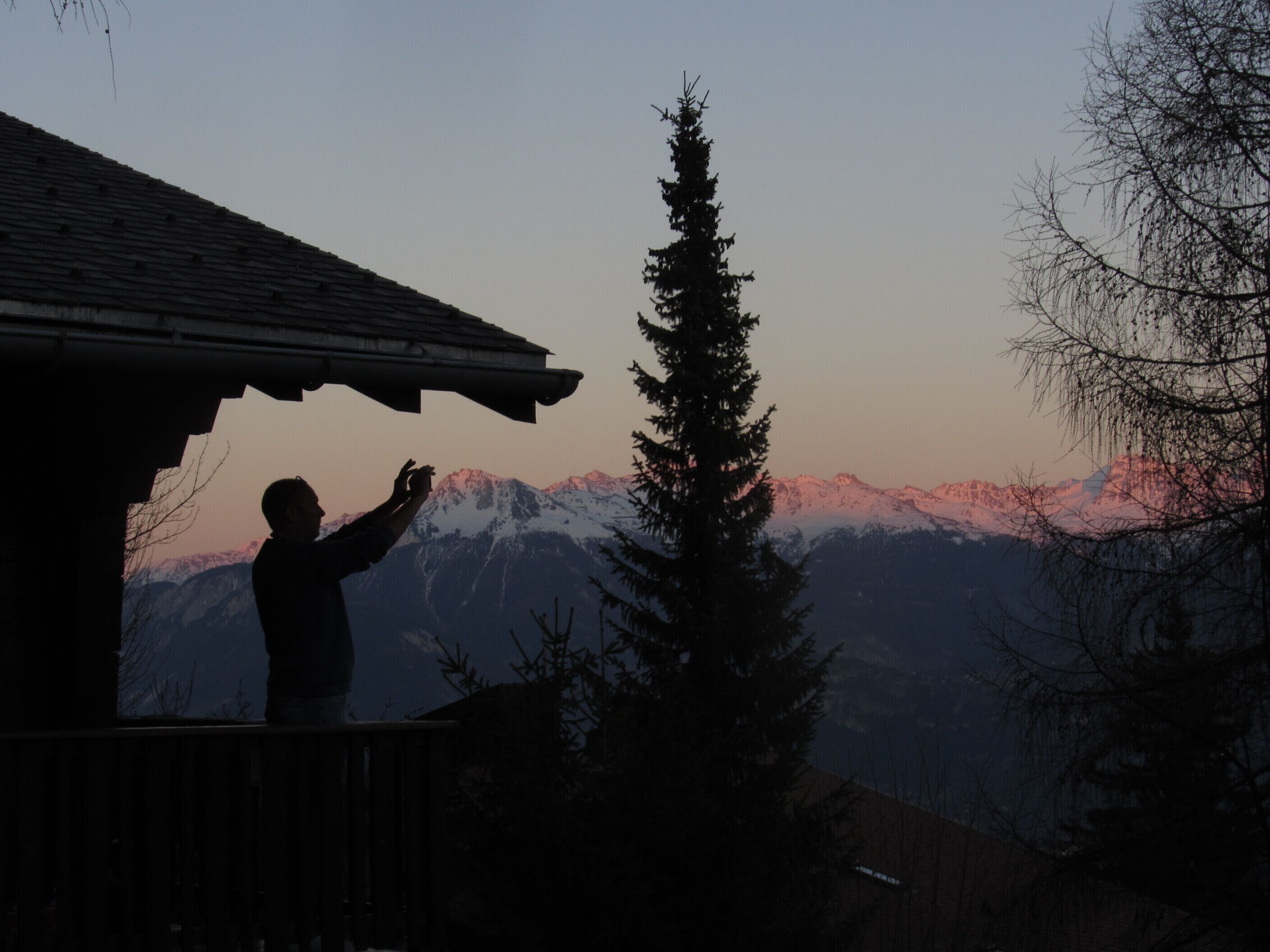 A person standing on a balcony overlooking a mountain range with snow-capped peaks.
