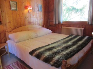 Une chambre dans une cabane en bois, avec un lit, une table de chevet, une lampe et une fenêtre avec des rideaux.