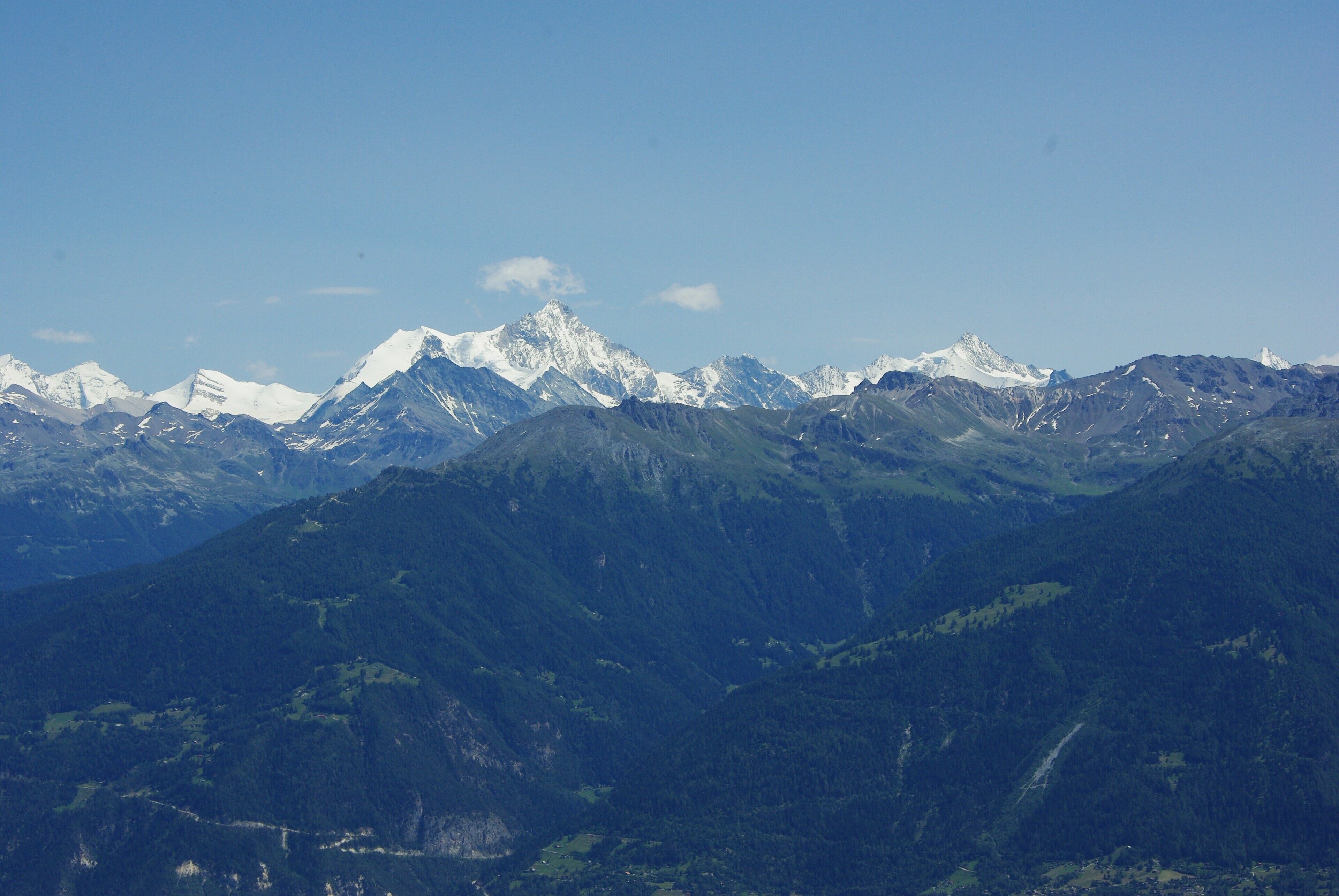 A mountain range with snow-capped peaks and dense forested valleys.