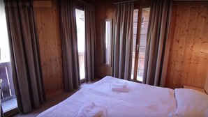 A wooden room with a bed, curtains, and a window.