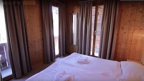Ein Zimmer mit Holzboden, einem Bett, Vorhängen und einem Fenster.