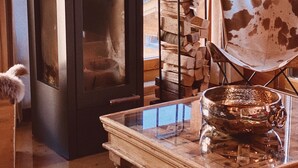 A cozy room with a fireplace, a glass table with a metal bowl, and a chair with a unique pattern.