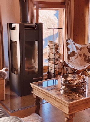Une pièce chaleureuse avec une cheminée, une table en verre surmontée d’un bol en métal et une chaise au motif original.