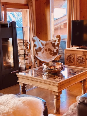 Ein gemütliches Wohnzimmer mit einem Glastisch, einem gemusterten Sessel und einem Fernseher auf einem Schrank.