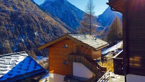 A wooden cabin with a sloped roof, surrounded by snow-covered mountains and a clear sky.
