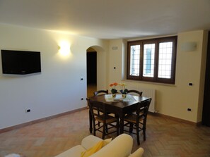 A dining area with a table, chairs, a TV mounted on the wall, and a window with blinds.