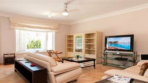 A living room with a sofa, coffee table, TV, and glass shelves. - Villa Meloneras Hills 16 Holiday Rentals (San Bartolome de Tirajana)