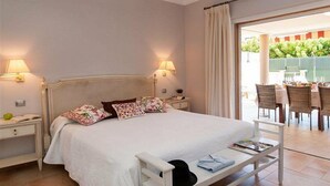 A bedroom with a bed, bedside tables, a nightstand, a reading stand, and a view of an outdoor dining area. - Villa Meloneras Hills 16 Holiday Rentals (San Bartolome de Tirajana)