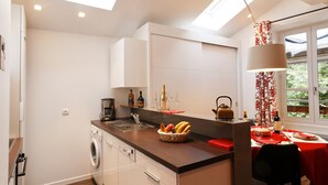 A modern kitchen with a built-in washing machine, a dining area with a red tablecloth, and a window with a view of greenery. - Studio La Savoyarde 4 stars Vision Luxe for 2 people Annecy (Menthon-Saint-Bernard)
