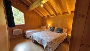 En stuga med träpanel, två sängar, ett fönster med gardiner, en värmare och en lampa.