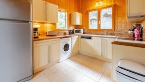Ett kompakt kök med träpanel på väggarna, vita skåp, tvättmaskin, mikrovågsugn och kylskåp.