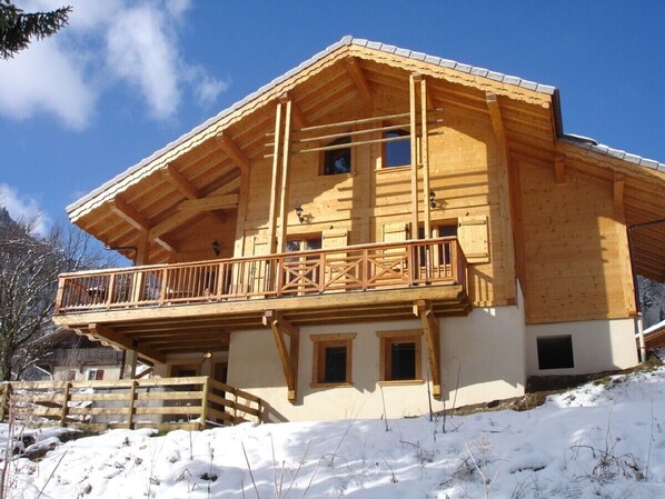 A wooden chalet with a balcony, a sloped roof, and a snow-covered ground.