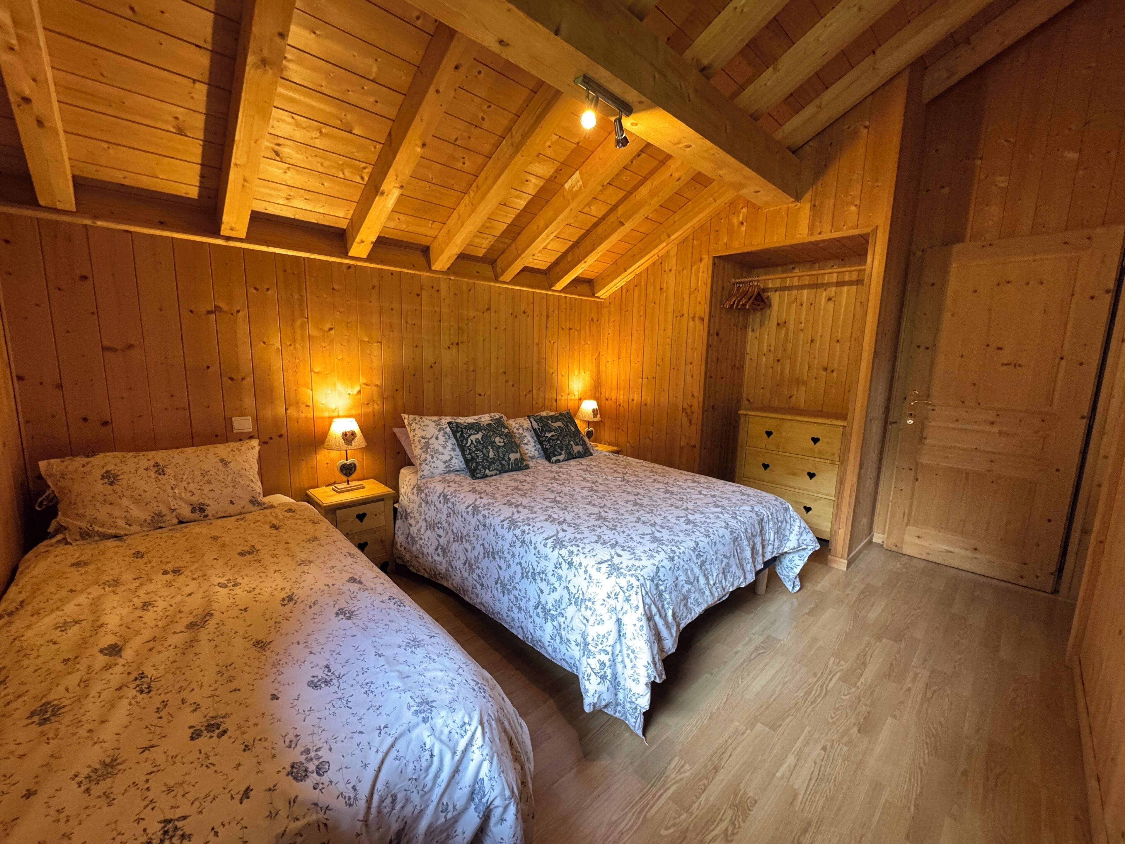 Een houten kamer met twee bedden, nachtkastjes met lampen, een kapstok en een deur.