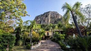 A pathway leading to a building with a mountain backdrop, surrounded by lush greenery and a small pool. - Luxury SPA Villa with Private Pool, Jacuzzi,Pine Forest - Available for Weddings (Partinico)