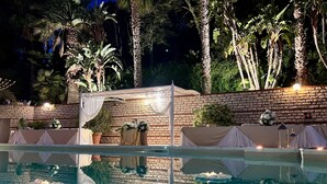 A pool area with a covered seating area, surrounded by palm trees and a brick wall. - Luxury SPA Villa with Private Pool, Jacuzzi,Pine Forest - Available for Weddings (Partinico)
