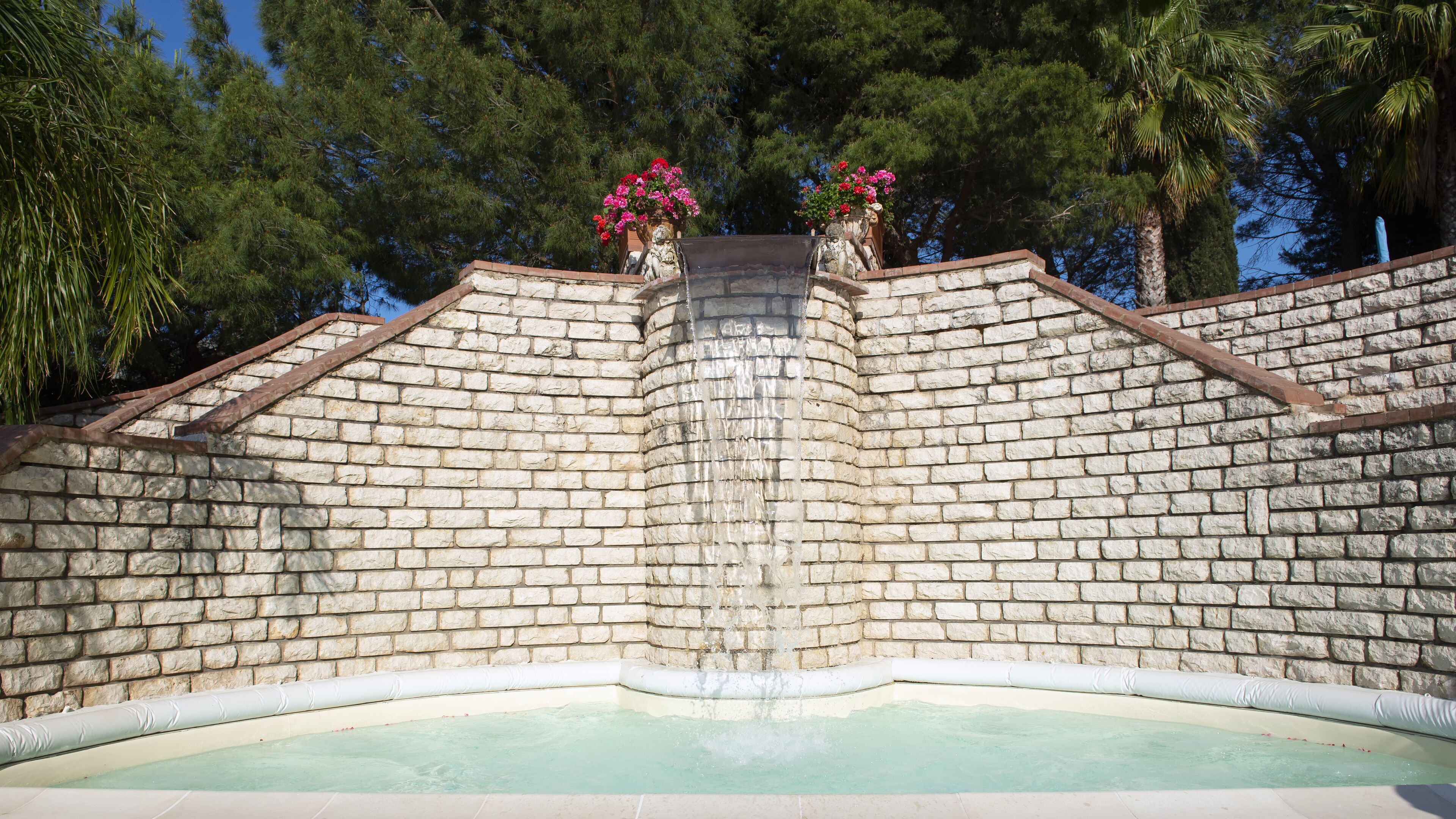 Une fontaine en pierre avec un bassin, entourée d’arbres.