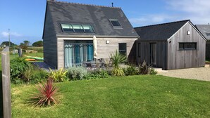 A modern house with a sloped roof, a patio with outdoor furniture, and a well-maintained garden. - Wooden house, close to beaches and dunes (Landéda)